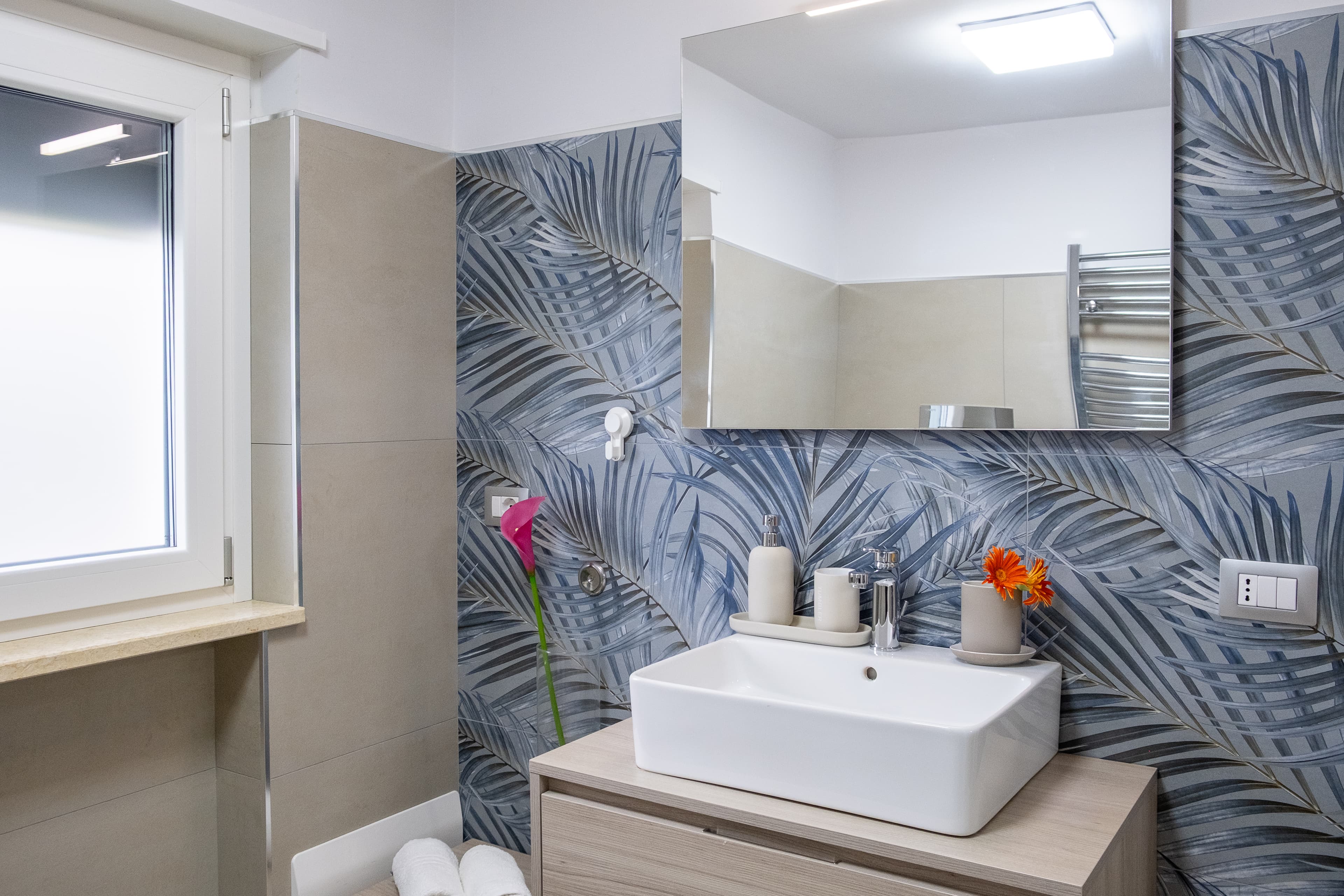 Bagno moderno — Ambiente elegante con lavabo ampio, specchio e piastrelle a tema tropicale